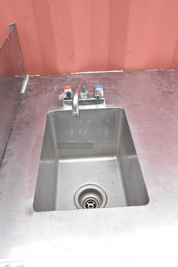 Stainless steel sink with dual-handle faucet, slightly worn condition, signs of use on surface, ideal for commercial settings.