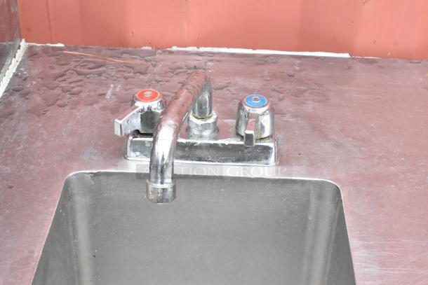 Stainless steel sink with dual-handle faucet, labeled hot and cold, showing signs of wear on countertop. Brand: Krowne.