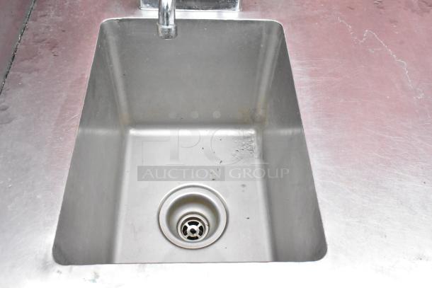 Stainless steel commercial sink, rectangular basin, clean with minor wear, integrated faucet, suited for heavy-duty use.