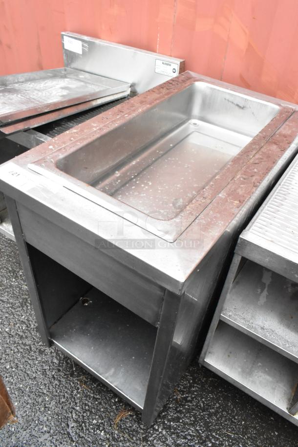 Stainless steel industrial sink with a deep basin and open storage below, visible wear and surface marks, Krowne label.