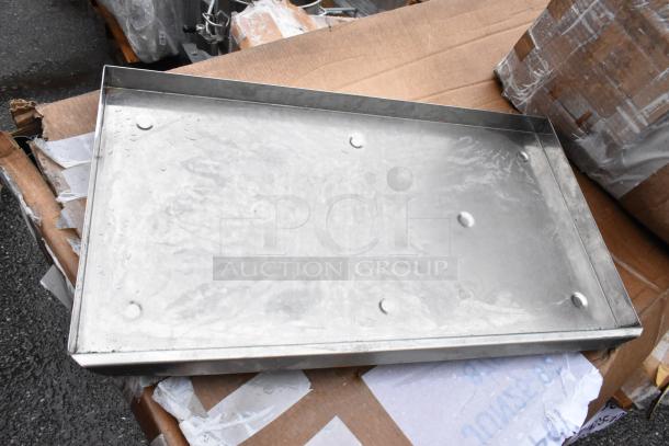 Metal tray with raised edges, rectangular shape, in used condition, displayed on cardboard boxes. No visible labels or markings.