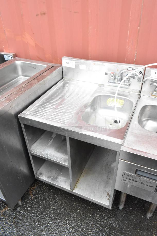 Stainless steel commercial sink with faucet, integrated drainboard, open storage, and "Hand Wash Station" label. Used condition.