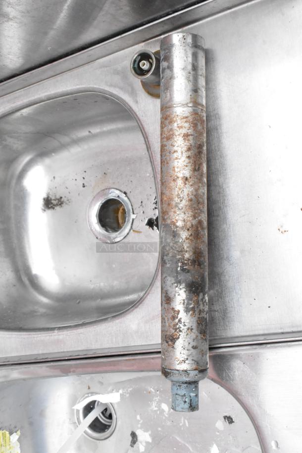 Rusty metal cylinder with blue cap, shown on stainless steel surface with visible rust and wear, indicating age and use.