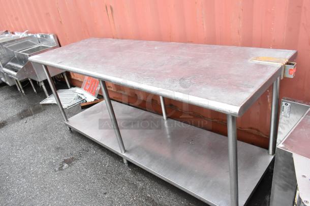 Stainless steel worktable with lower shelf, four legs, slight surface wear, located outdoors, no visible markings.