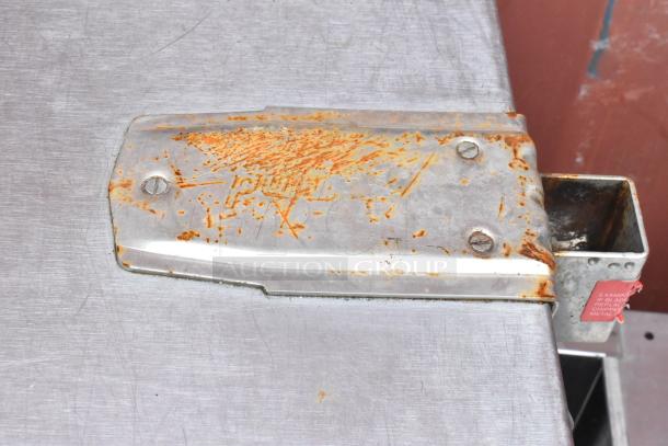 Rusty metal tool with bolts and a rectangular extension, showing wear and rust. Tag reads: "Examine blade, replace if chipped."