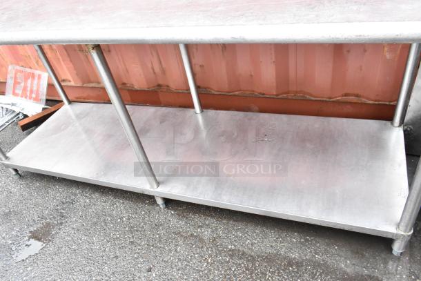Stainless steel kitchen prep table with two tiers, showing signs of wear, suitable for commercial use.