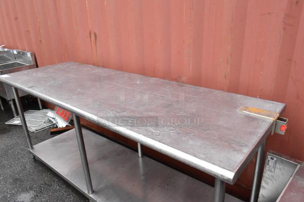 Stainless steel industrial work table with a worn surface, shelf below, and minor signs of rust. No visible labels.