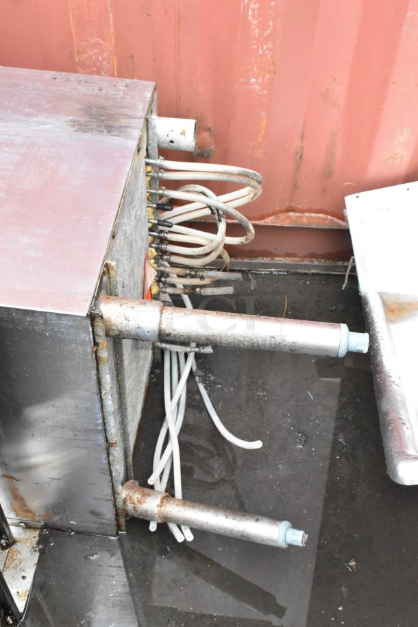 Industrial metal cooling unit with attached hoses, showing rust and wear, in used condition. No visible labels or markings.