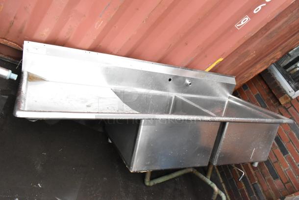 Stainless steel double basin industrial sink, good condition, with faucet holes, minor wear visible.