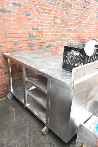 Stainless steel commercial work table with wheels, shelves, and storage compartments; moderate wear; ideal for kitchen use.