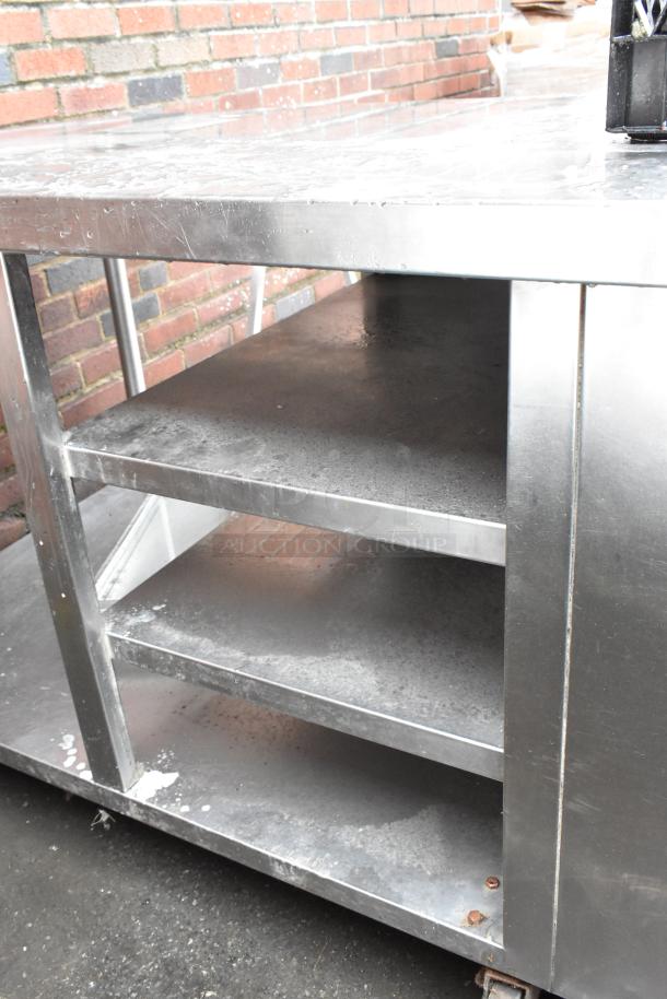 Stainless steel kitchen prep table with three shelves, shows signs of use, suitable for commercial kitchens.