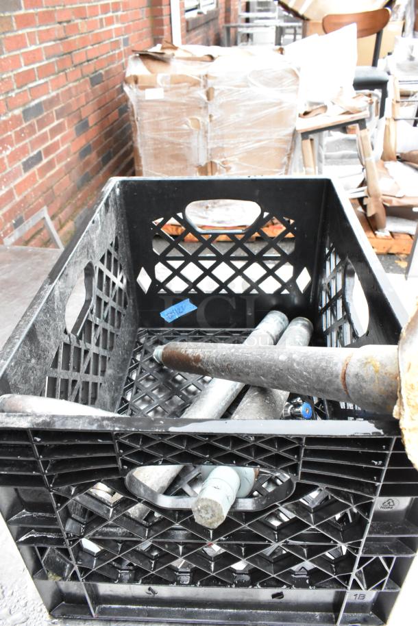 Black crate containing metal pipes, some rusted, on an outdoor surface. Crate marked with a small blue label "9912."