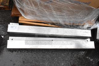 Two aluminum rectangular beams, wet surface, placed on a pallet. Visible tag reads "233" indicating auction lot number.