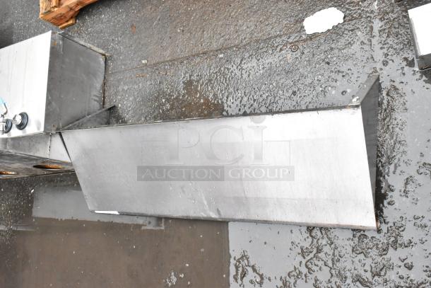 Stainless steel rectangular sink with dual faucets, shown in used condition with visible wear on a wet concrete surface.