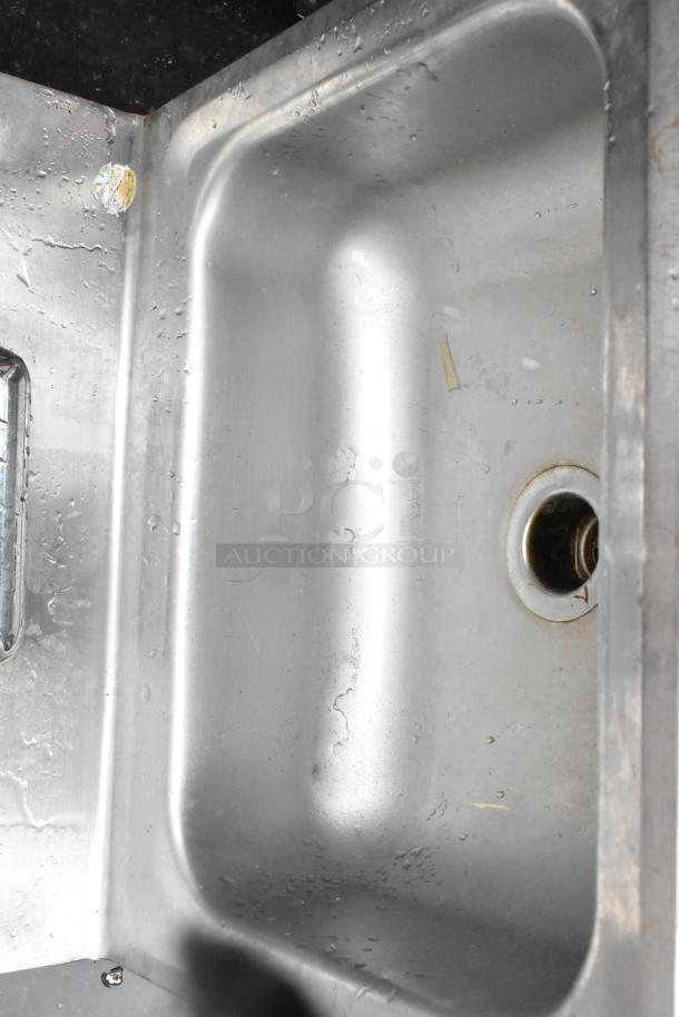 Stainless steel kitchen sink, used condition with water spots. Features a single basin and drain opening, no visible brand markings.