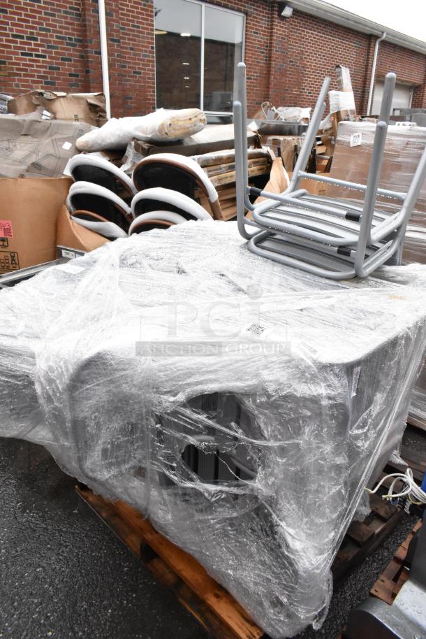 Plastic-wrapped stack of gray metal chairs on a pallet, protected for transportation. Boxes and wrapping in the background.