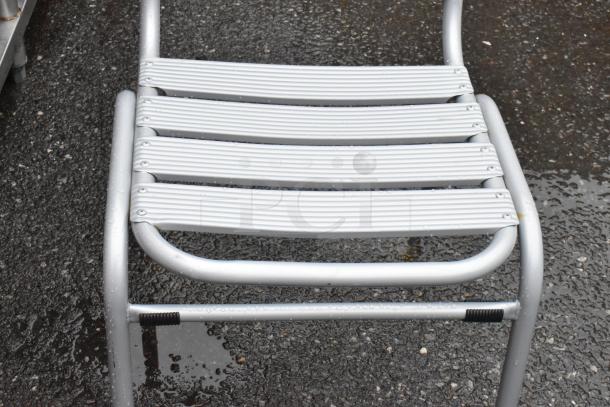 Silver metal chair with slatted seat, wet from rain, outdoors. Some visible wear but overall good condition.