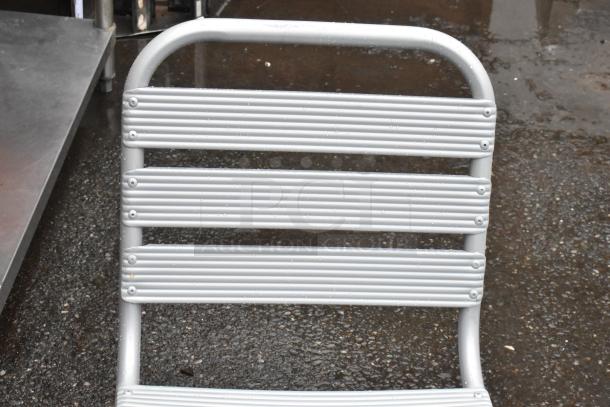 Aluminum folding ladder with four rungs and a curved top handle, shown on wet pavement, in used condition.