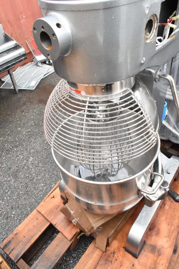 Industrial stand mixer on pallet, metal body with whisk attachment, stainless steel bowl, used condition.