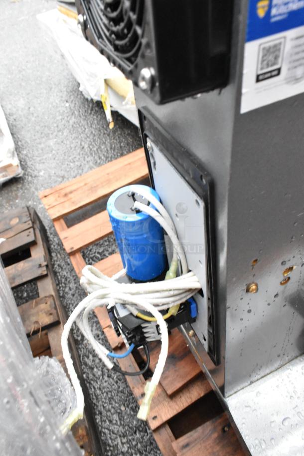 Metal industrial machine on a pallet, featuring a blue component with wires. Tags and labels appear for technical specs.