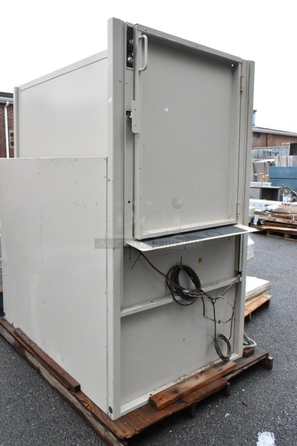 Large industrial metal cabinet with front door, wiring visible, placed on a wooden pallet. Some wear visible on the surface.
