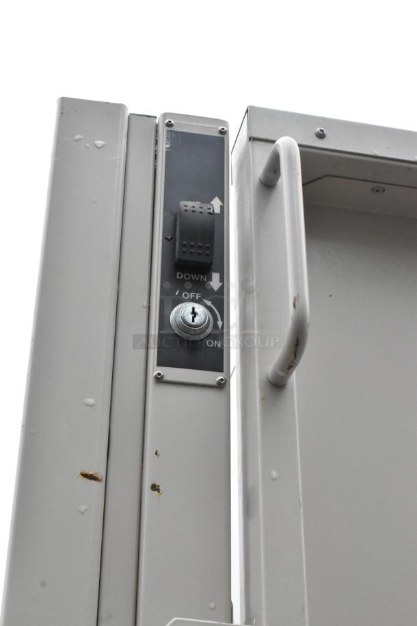 Vertical platform lift with control panel, featuring a toggle switch for up/down and keyhole for on/off. Visible rust spots indicate wear.