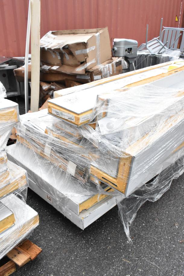 Pallets of metal panels wrapped in plastic, some boxes damaged, labels suggest steel shelving components.