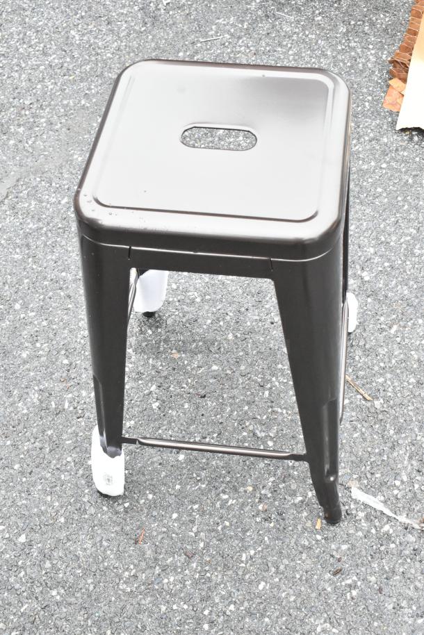 Metallic square stool with a hole in the seat for easy handling, in good condition, protective foot coverings visible.