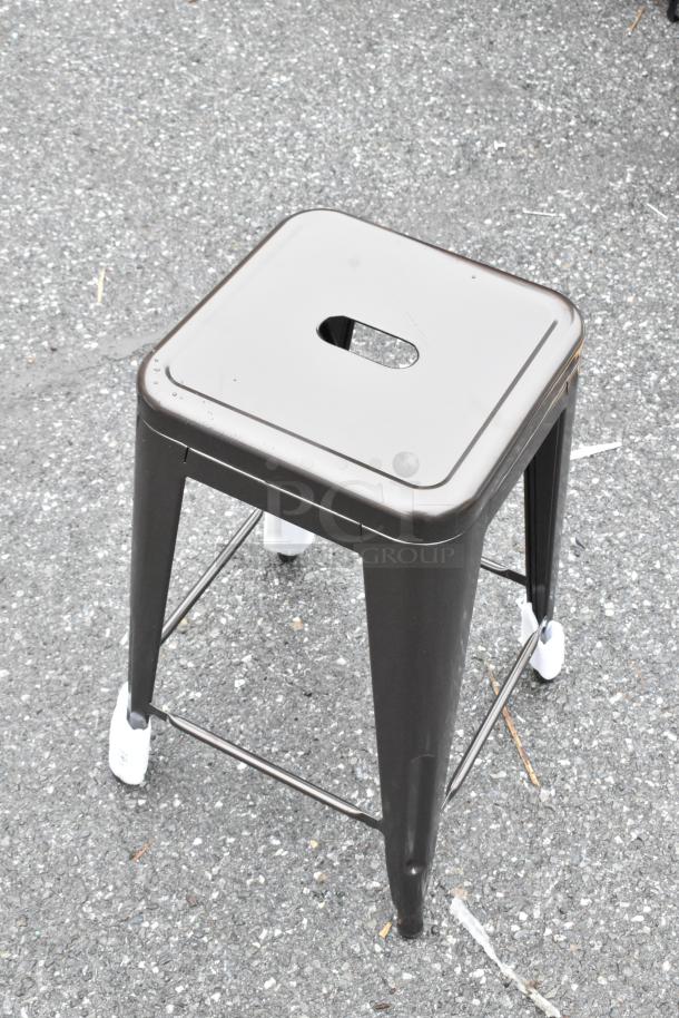 Metal square stool with a cutout handle, gray finish, and protective foot caps. Slight wear visible, good condition.