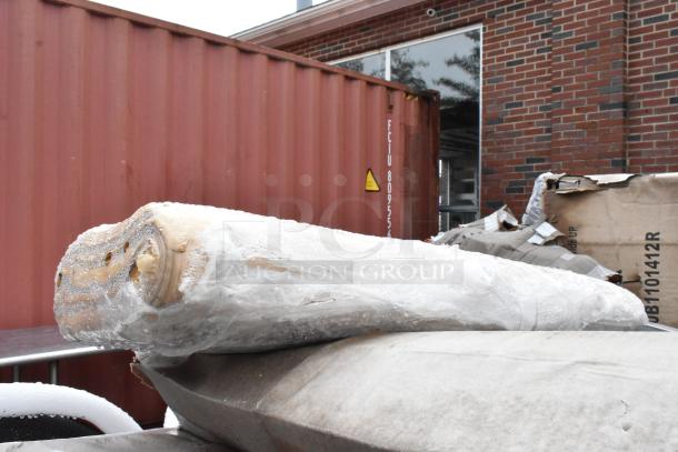Rolled fabric wrapped in plastic, slightly damp, positioned in an industrial outdoor area with a shipping container in the background.