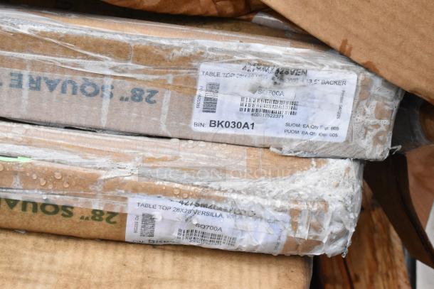 Stacked 28x28-inch table tops in packaging with clear labels; shows model SQ700A, bin BK030A1, covered in protective wrap.