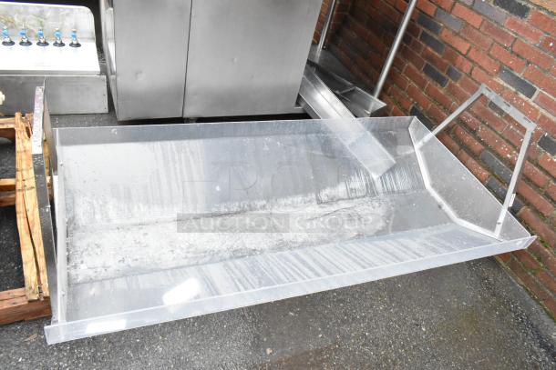 Large clear acrylic tray with angled sides, slight surface wear, next to metal equipment and brick wall, no visible markings.