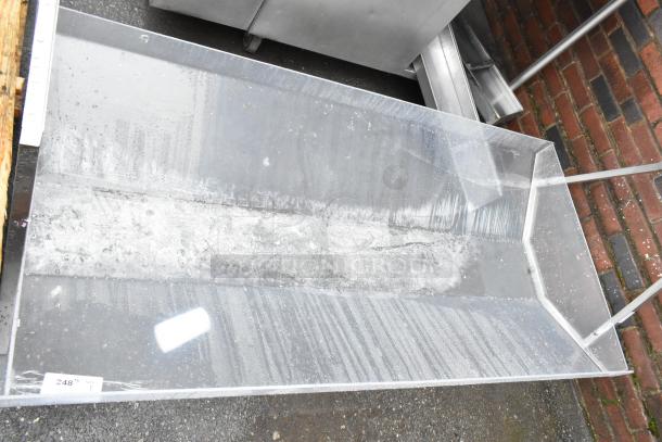 Large transparent acrylic display holder, slightly scratched, with a white label reading "248." Positioned on a paved surface.