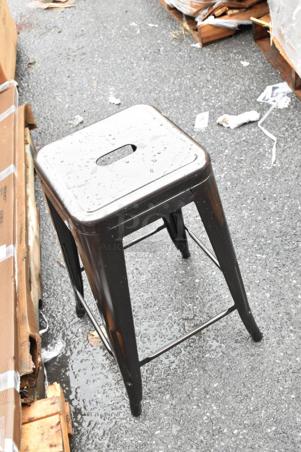Black metal stool with cut-out handle, square seat, and four legs. Some water droplets visible; used condition.