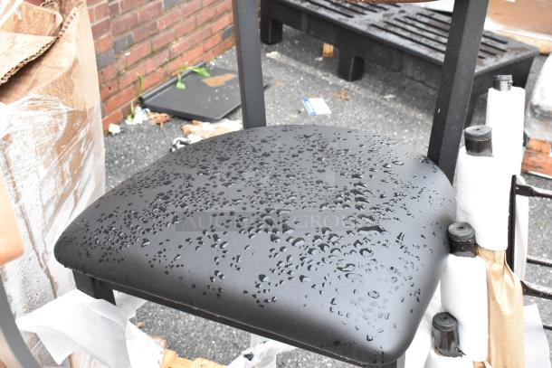 Black metal chair seat with water droplets, outdoor setting. Seat is attached to a partially visible chair frame.