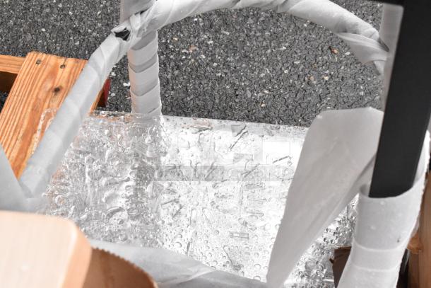 Wrapped ice sculpture on wooden pallet, partly covered with protective material, on asphalt background.
