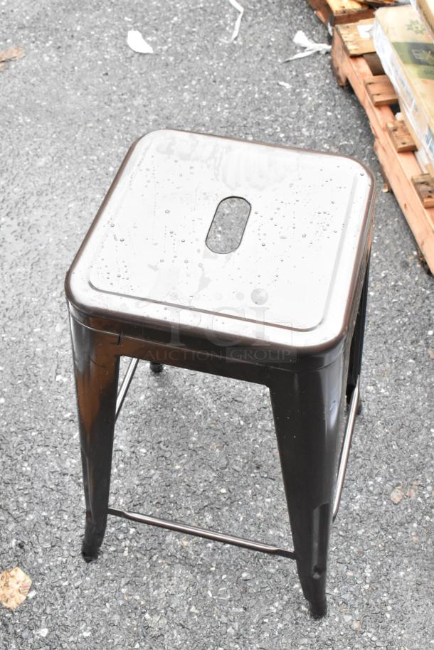 Industrial metal stool with a square seat and a cutout handle, showing water droplets, in used condition.