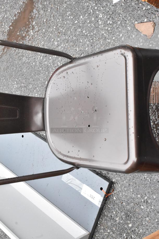Metal chair with brown finish, visible raindrops on seat, minor wear, placed on gravel. Label with unclear details visible.
