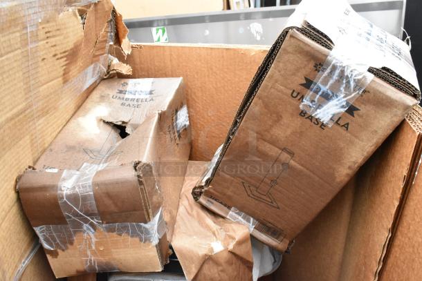 Damaged boxes of umbrella bases in a cardboard container, with visible tears and tape, labeled "Umbrella Base."