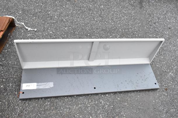 Gray metal shelf with a rear backplate, visible barcode tag marked "253", showing minor wear on the surface.
