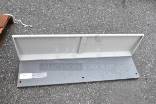 Gray metal shelf with a rear backplate, visible barcode tag marked "253", showing minor wear on the surface.