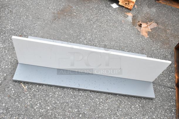 Rectangular metal part, gray finish, slight water spots, laid on rough pavement, no visible markings or labels.