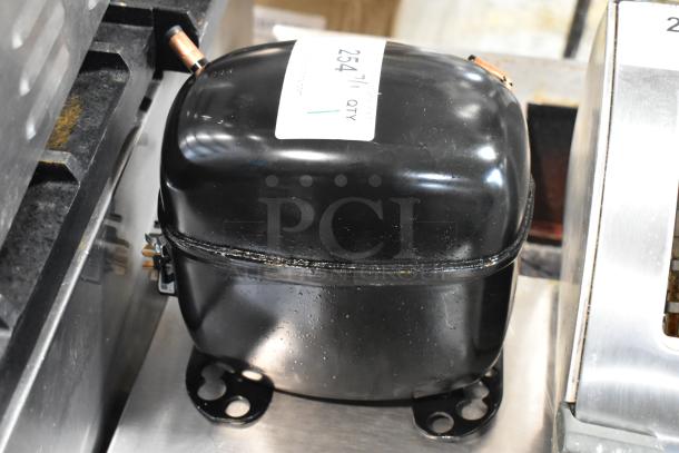 Black compressor unit with attached copper pipes, in good condition. Label reads "254/1 QTY." Used in refrigeration systems.