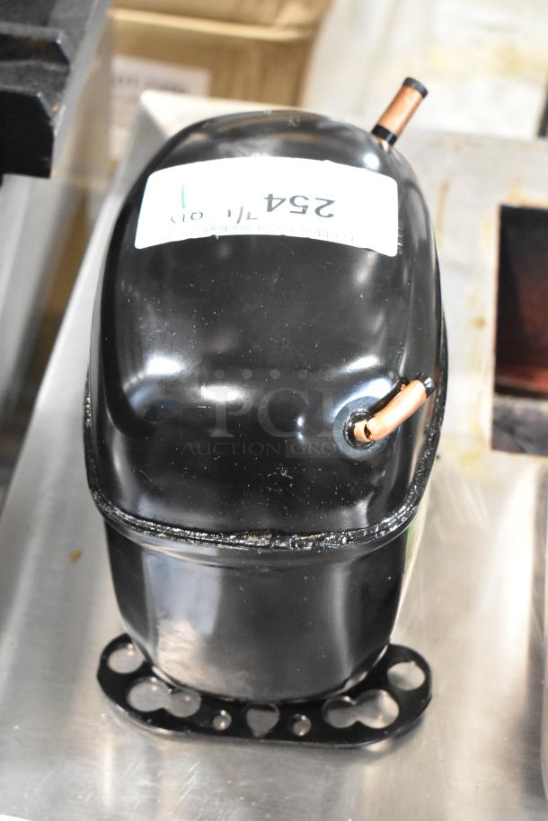 Black refrigeration compressor with copper tubing, labeled "254T." In good condition, mounted on a metal base.