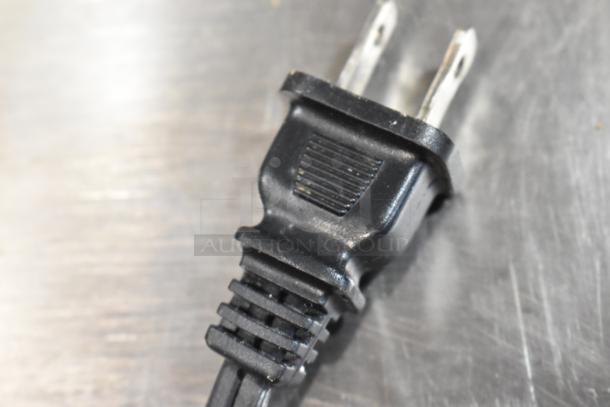 Close-up of a black electrical plug with two prongs on a metallic surface. Good condition, no visible labels or markings.
