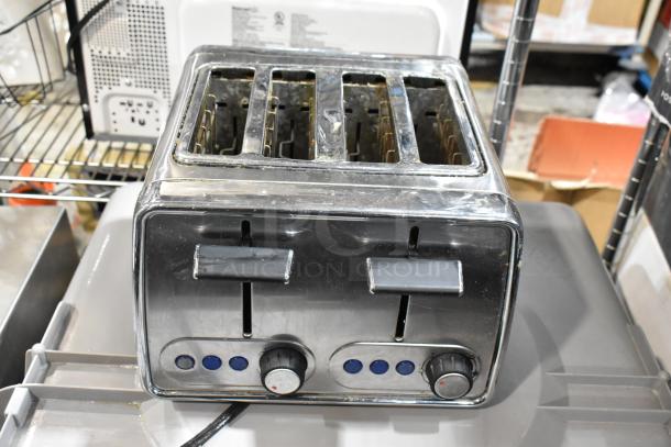 Stainless steel four-slice toaster with dual controls and blue indicator lights. Shows signs of wear, includes dial knobs.