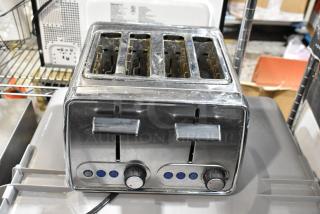 Stainless steel four-slice toaster with dual controls and blue indicator lights. Shows signs of wear, includes dial knobs.