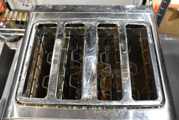 Four-slot metal toaster with visible wear and residue in slots, indicating used condition. No visible brand markings.