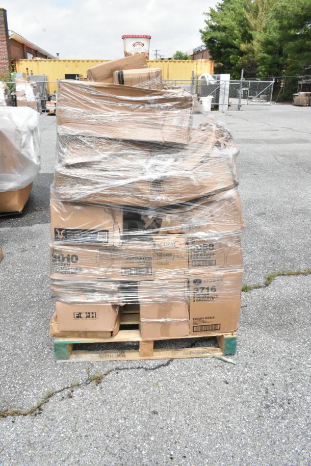Pallet of assorted cardboard boxes wrapped in plastic, showing various labels for glasses, stacked outdoors on pavement.