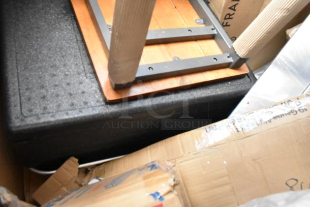 Stacked wooden and metal table parts on a protective frame, surrounded by cardboard packaging. Labels indicate fragile contents.